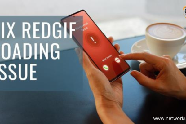 A person’s hand holding a smartphone with an on-screen message “FIX REDGIF LOADING ISSUE” against a blurred background featuring a laptop and a cup of coffee.